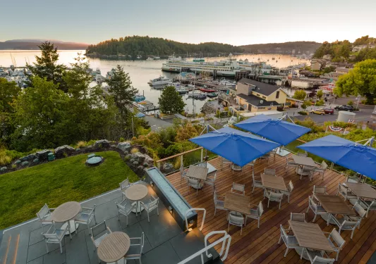 Exterior view of an outdoor patio with large blue umbrellas and a lake in the background