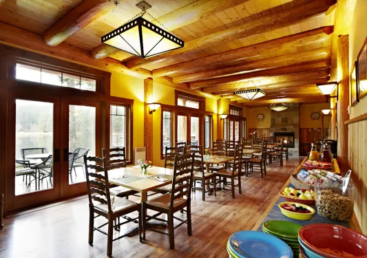 Cabin dining hall with wooden tables and chairs, with breakfast foods along the walls