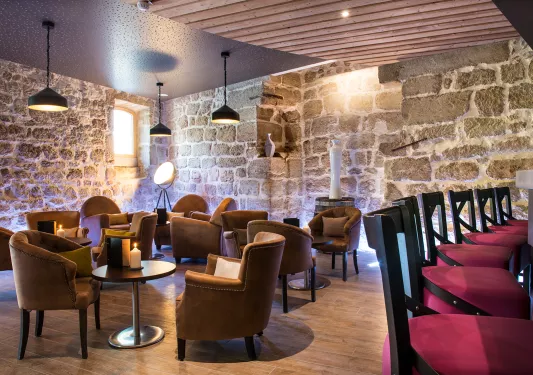 Tavern with cushioned chairs and circular tables, with stone walls