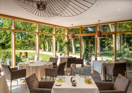 Dining room with cushioned chairs and white tables, in a room with large windows