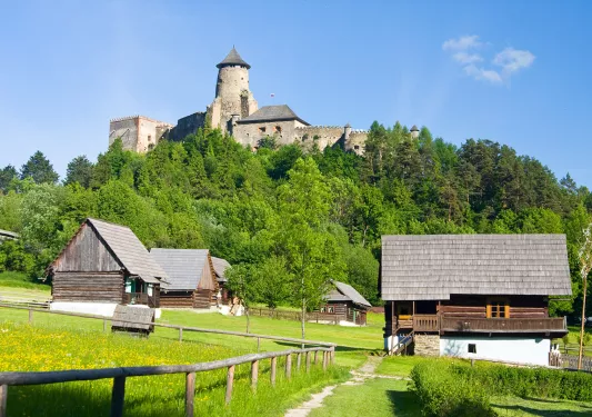 Barns on a green filed below a mountain with a castle on it