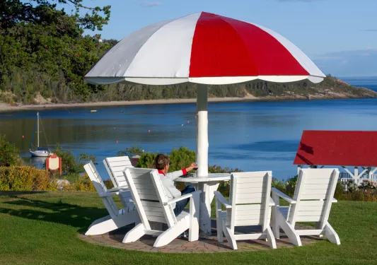 Person sitting on a white lawn chair in front of a red and white table, looking out to the ocean