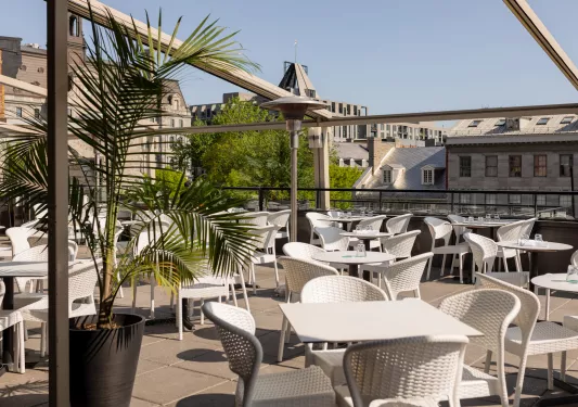 Outdoor patio with white tables and chairs, with town buildings in the background
