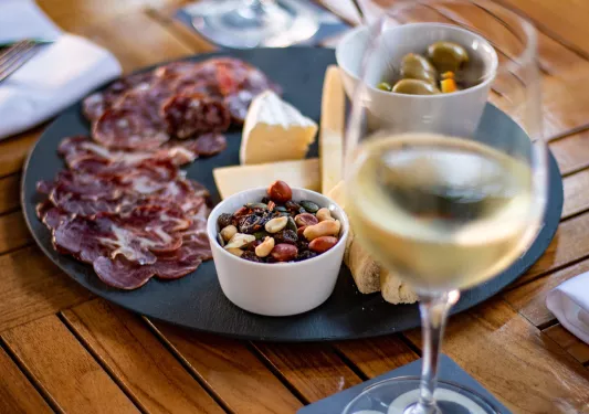 Plate with cured meats, nuts and cheese next to a glass of wine