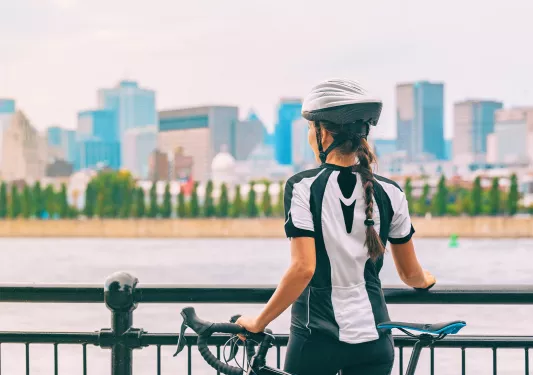 Woman standing next to her bike, looking out to a city and a river