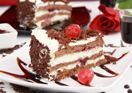 Chocolate cake on a white plate with red cherries on top