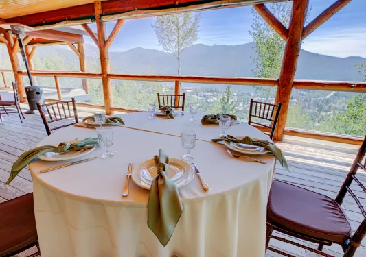 Circular dining table on an outdoor patio, overlooking a small town and tall trees