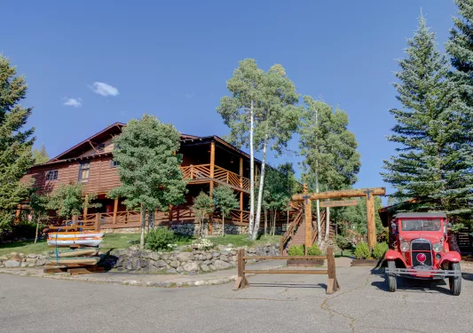 Exterior view of large cabin building with tall trees and a stone fence