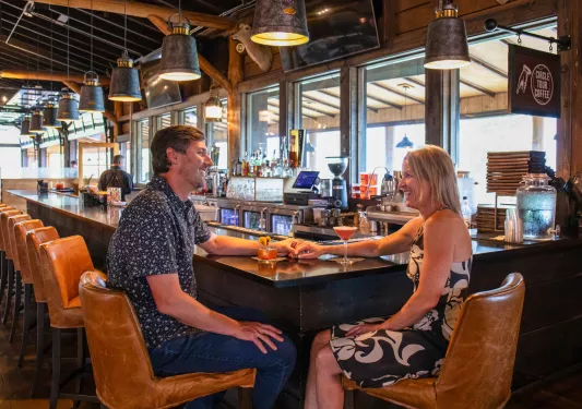 Man and woman smiling and holding hands while sitting at a bar