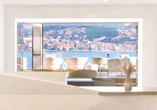 Cushioned white chairs on an outdoor patio looking out towards a large lake a distant town