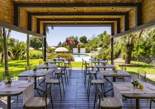 Outdoor patio with rows of dining tables and chairs, with an outdoor pool in the background