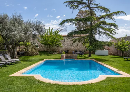Outdoor pool with a large grass field and tall trees in the back