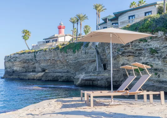 Two reclining chairs under an umbrella on the sand, on a beach