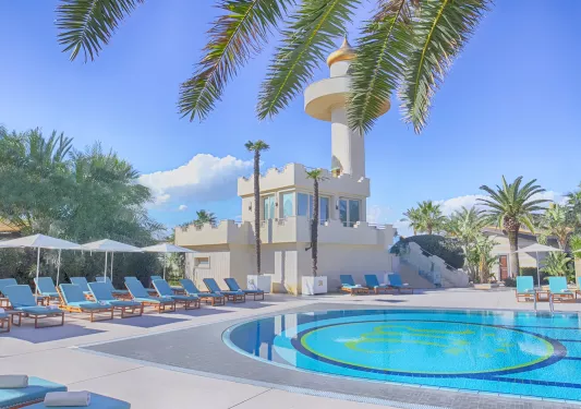 Exterior view of white building and an outdoor pool, surrounded by white chairs