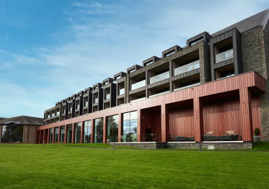 Exterior view of a long red and black building, with a grass field in front