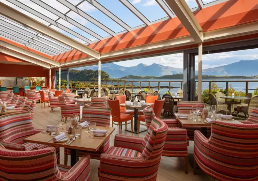 Outdoor dining area of a restaurant with striped red, cushioned chairs and square dining tables