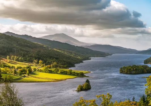 Large river next to a grassy valley covered in trees