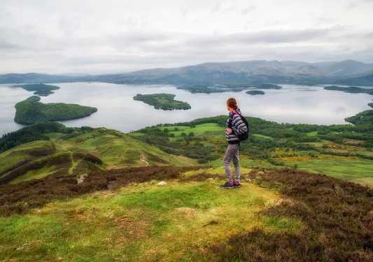 Woman standing on top of a grassy hill, looking out to smaller hills