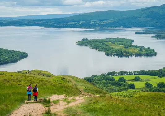 Two people descending a grassy hill towards a large lake