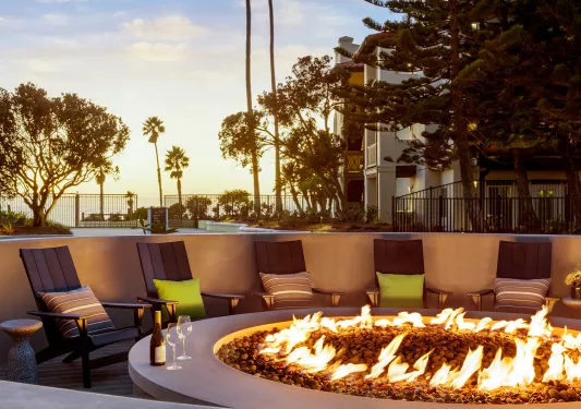 Outdoor firepit with chairs surrounding the pit, with trees and a sunset in the background