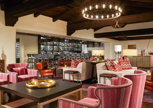 Bar and lounge with red, cushioned chairs and an alcohol shelve in the back