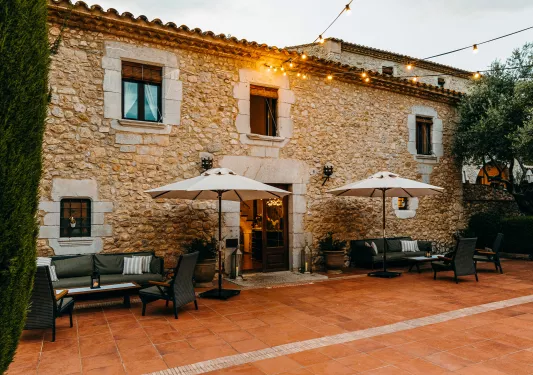 Exterior view of stone building with gray chairs and umbrellas in front