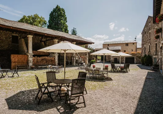 Outdoor area with dining tables covered with umbrellas, and stone buildings surrounding
