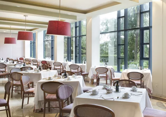 Dining hall with white, square tables and cushioned wooden chairs