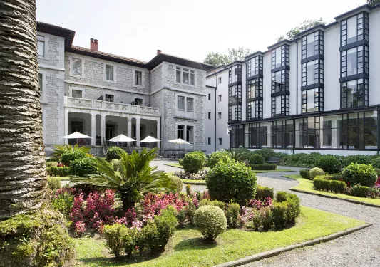 Exterior view of white, black and gray stone hotel building with a garden in front