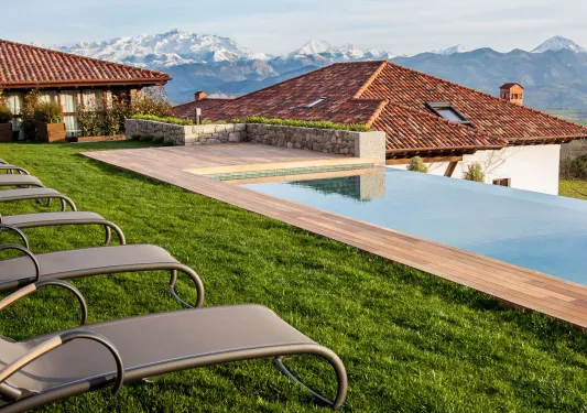Outdoor pool surrounded by grass, gray reclining chairs and buildings in the background
