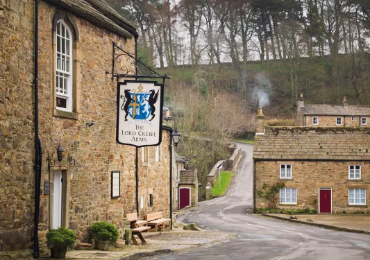 Rustic, stone building with a sign in front, with a forest in the background
