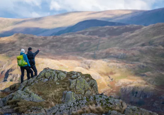 Two people standing on top of a cliff pointing towards smaller hills