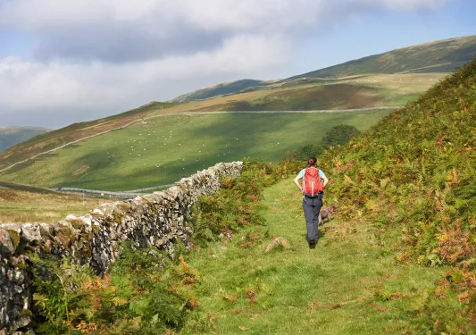 Woman walking on a grass trail looking towards large hills