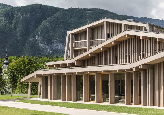 Exterior view of wooden building with tree-covered hills in the background