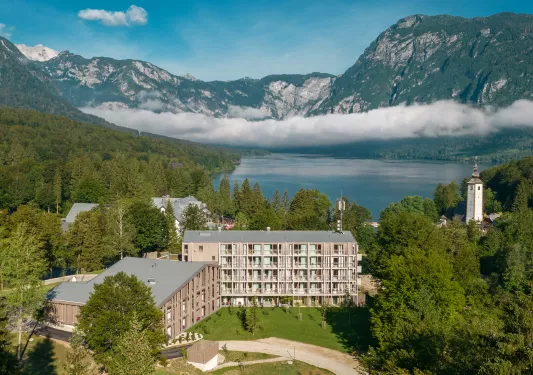Exterior sky view of a large wooden hotel building with a large lake and mountains in the background