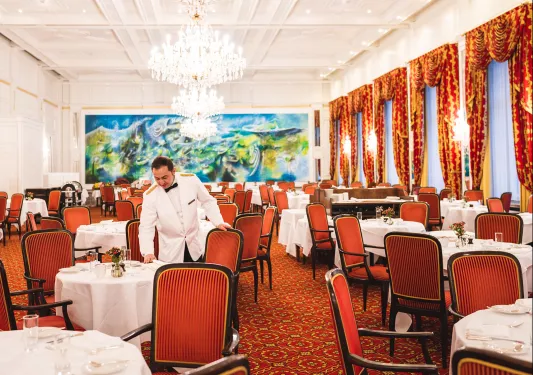Dining hall with a waiter arranging red chairs around circular white tables