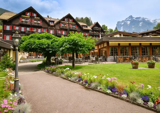 Exterior view of large brown and beige hotel building, with a grass area and small trees in front