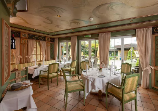 Restaurant with a painted ceiling of flowers, and green tables around tables with white cloths