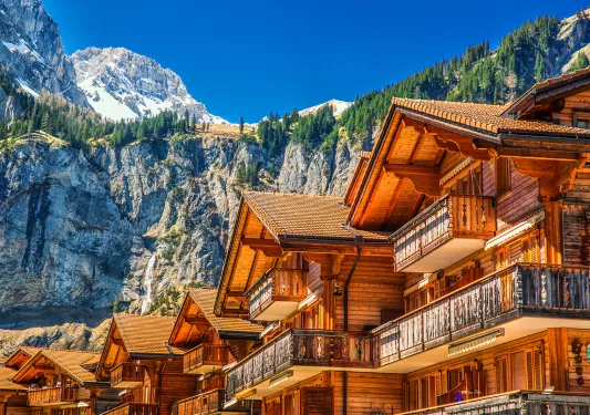 Row of wooden cabin buildings, with large mountains in the background