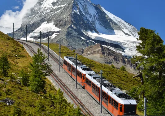 Train going down a hill, with snow-capped mountains in the distance