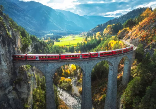 Red train on a railway on a bridge multiple stories above ground