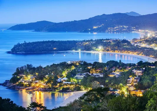 Sky view of city illuminated by lights, with the ocean in the background