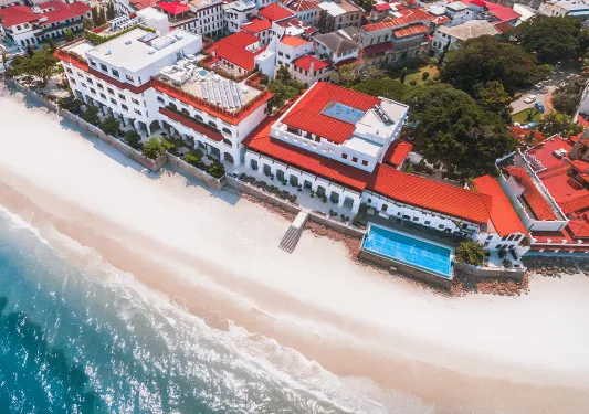 Sky view of large, white hotel complex with red roofing and the beach in front