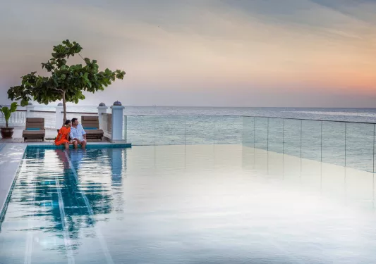 Outdoor infinity pool, with man and woman sitting with their feet in the pool