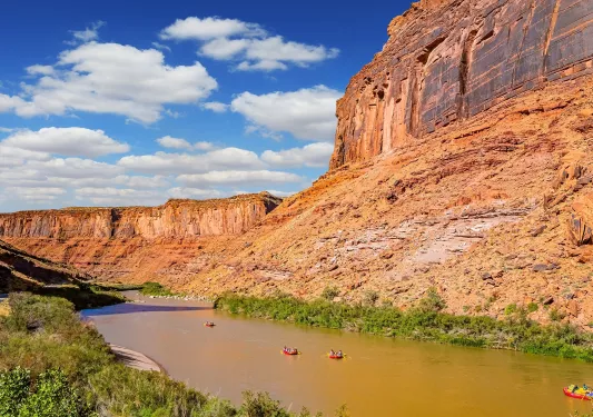 Large river next to a canyon, with people in red rafts paddling through the river