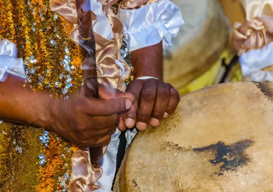Person's hands holding a stick and playing a set of bongos