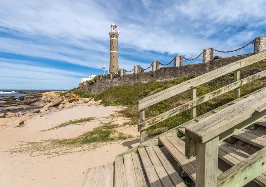 Beach with a wooden staircase and a lighthouse in the background