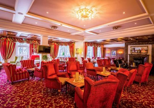 Large hall and seating area with large, cushioned red chairs and a fireplace in the back