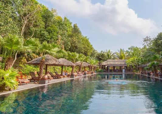 Outdoor pool surrounded by straw huts and reclining chairs