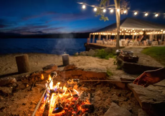 Outdoor firepit by the beach, with people roasting marshmallows on sticks